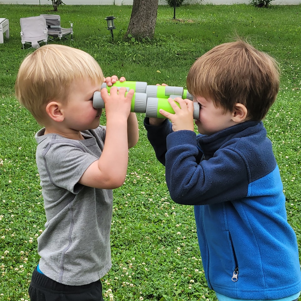 Two boys looking through binoculars at each other in the garden