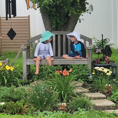Two children in sun hats chatting on a garden bench