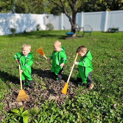 Children in green rain suits raking leaves in the garden