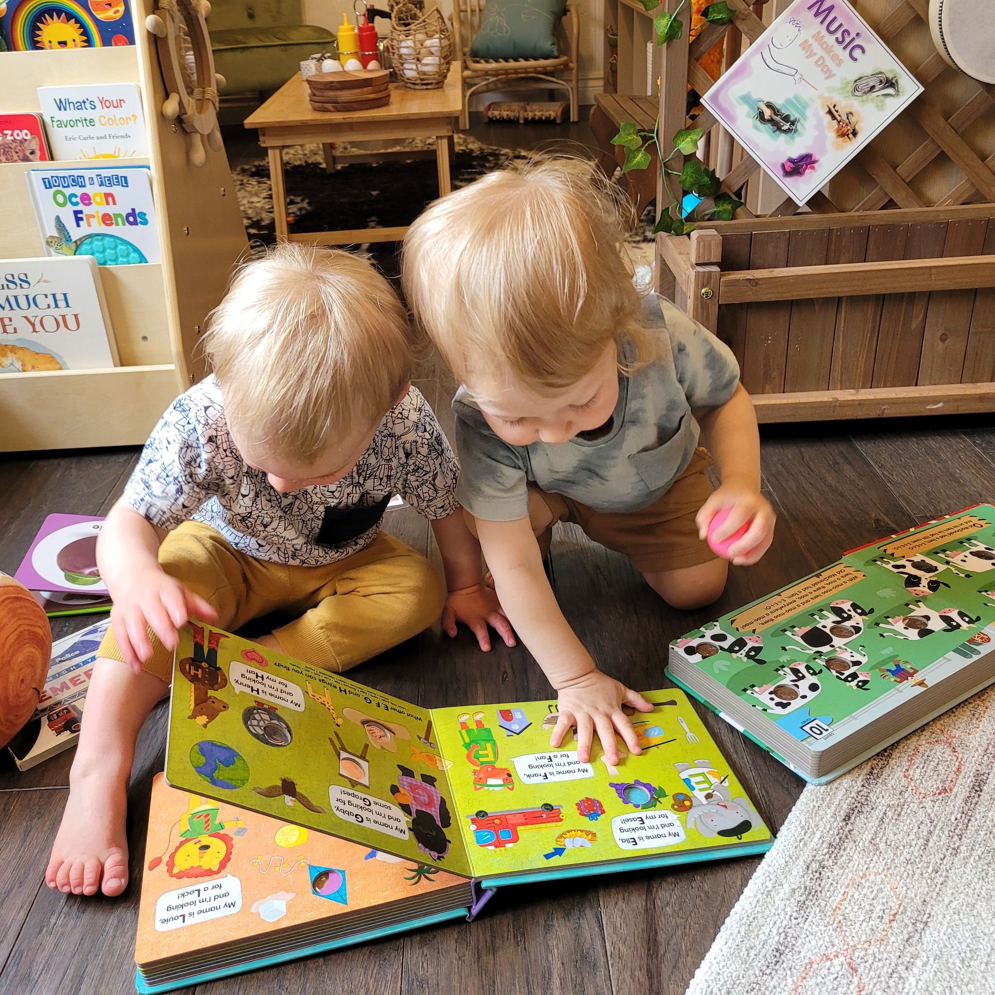Two toddlers sitting on the floor reading picture books together