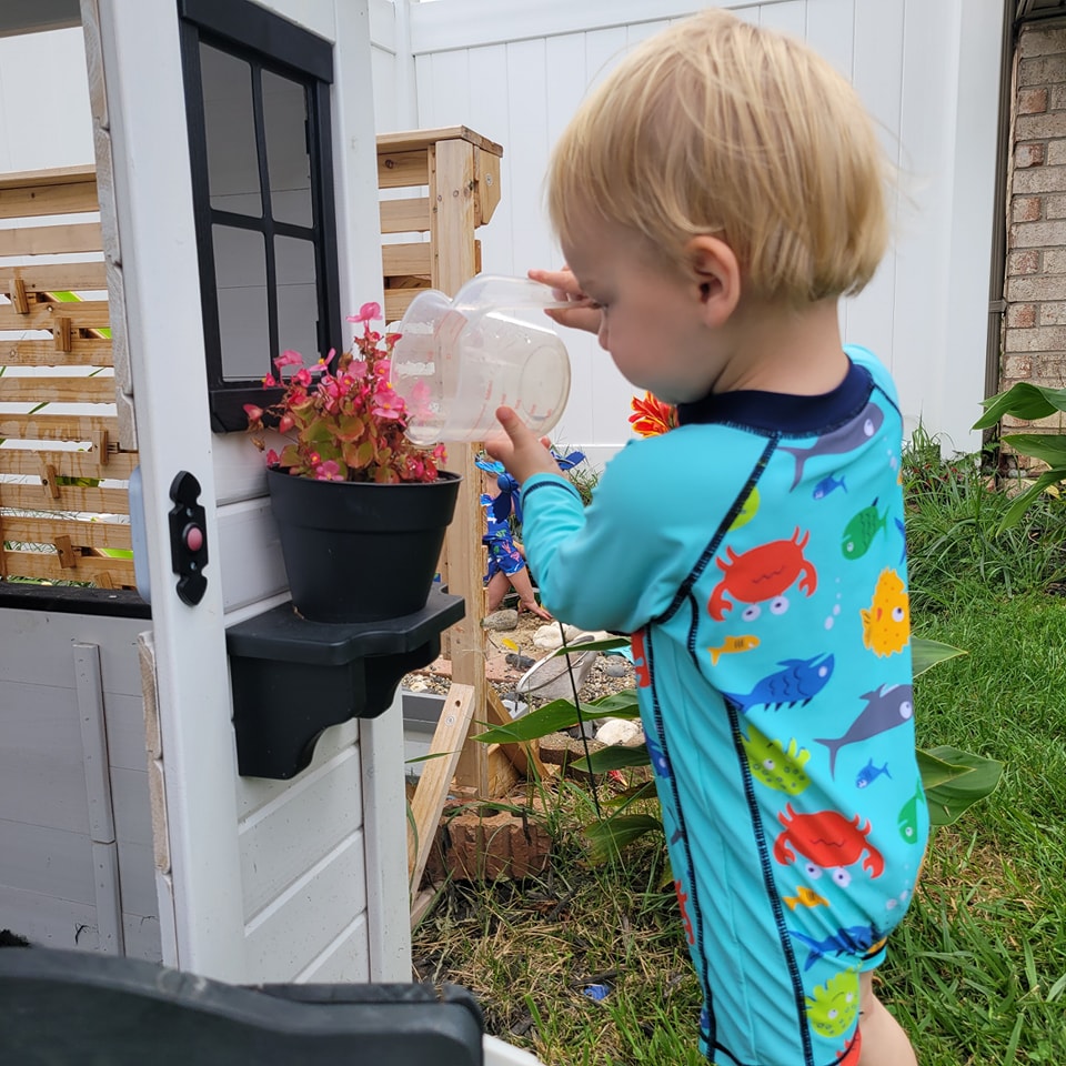 Boy watering flowers at the playhouse with a watering can